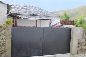 Propiedad amurallada con muro de piedra, portón metálico y una escalera que lleva a un edificio con tejado de baldosas.