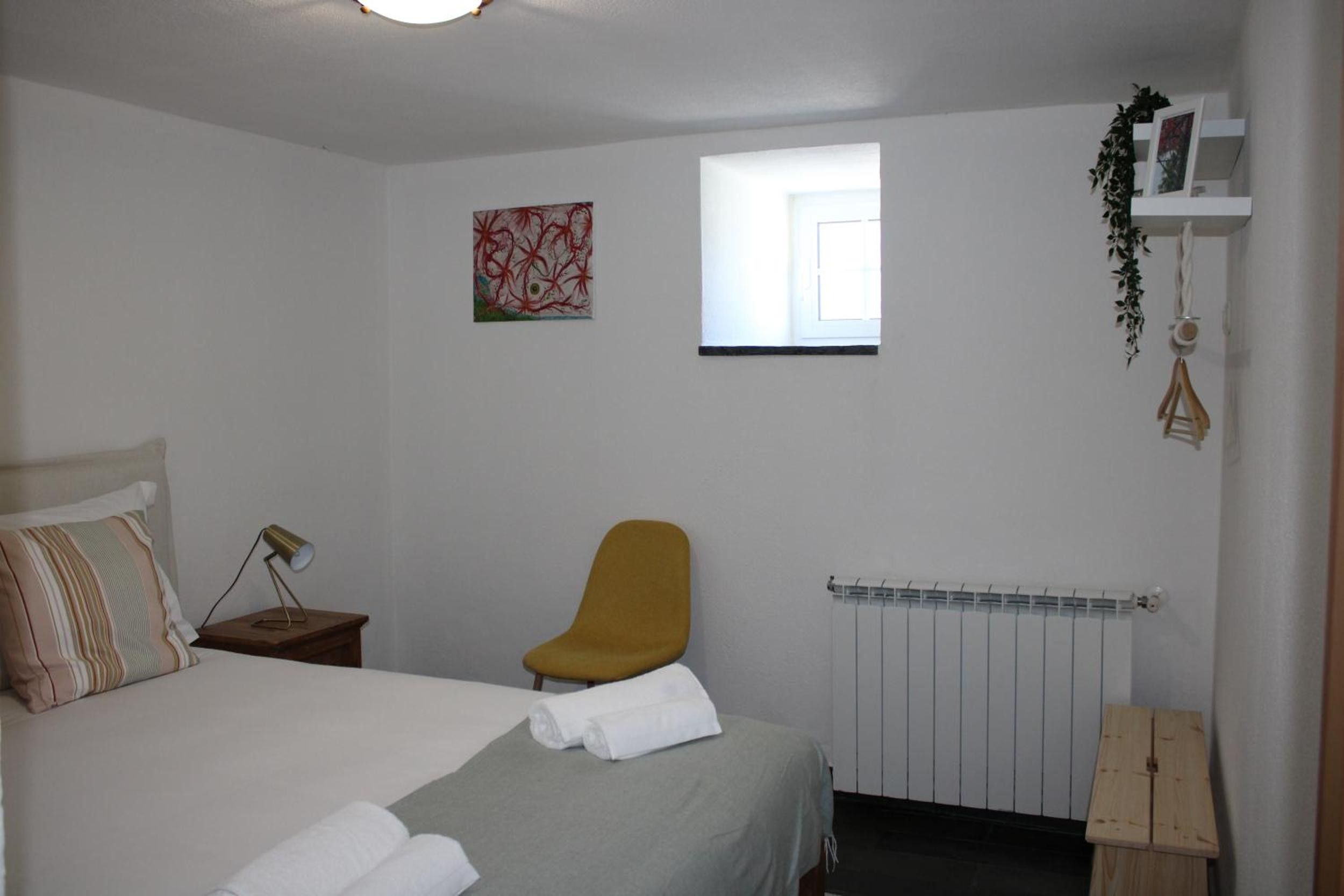 A bedroom with a bed, a chair, a radiator, a window, and a wall-mounted shelf with a plant.