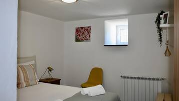 A bedroom with a bed, a nightstand, a chair, a radiator, and a window.