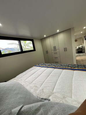 Ein Schlafzimmer mit Bett, Kleiderschrank und einem Fenster mit Blick auf Grünflächen.
