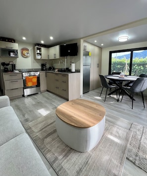 Une cuisine moderne dotée d’un four encastré, un coin repas avec une table ronde et des chaises, et une grande fenêtre offrant une vue sur la verdure.