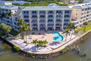 Ein mehrstöckiges Hotel mit Poolbereich, Palmen und Blick auf das Wasser.