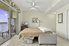 Ein Schlafzimmer mit Bett, Fernseher, Schreibtisch mit Stuhl und einem Balkon mit Blick auf das Wasser.