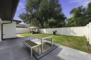 Eine Terrasse im Freien mit Tisch und Stühlen, einem überdachten Sitzbereich und einem weißen Zaun.