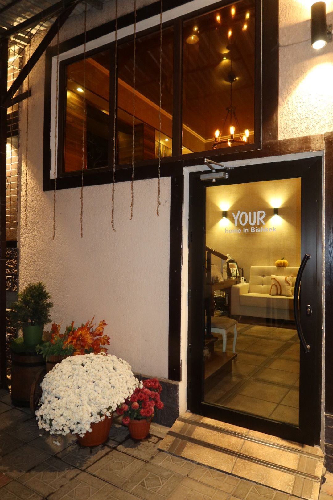 A hotel entrance with a glass door, a sign reading 'YOUR home in Bishkek,' and a sofa visible inside.