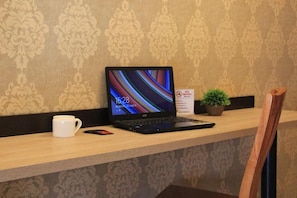 A laptop on a wooden desk with a white mug beside it, a small potted plant, and a 'No Smoking' sign. - Lavitor hotel (Bishkek)