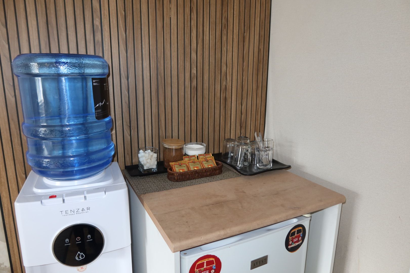 A water dispenser, a small refrigerator, and a tray with cups and condiments.