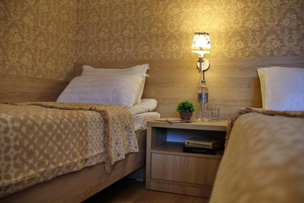 A hotel room with two beds, a nightstand with a lamp, a small plant, and a book titled 'The Art of War.'