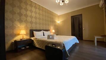 Una habitación de hotel con una cama, lámparas de noche, una computadora portátil, una maleta y una puerta.