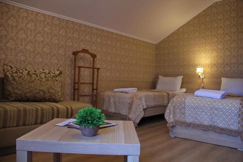 Una habitación con dos camas, un sofá, una mesa con una planta y una lámpara.
