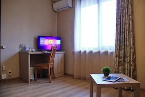 A room with a desk, chair, and a small table with a plant. There is a window with curtains and an air conditioning unit on the wall. - Lavitor hotel (Bishkek)