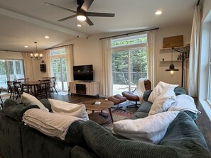 A modern living room with a sofa, coffee table, and a TV. There is a dining area with a table and chairs. - New 3BR House in Southwest Harbor! [Eagle`s Ledge] (Southwest Harbor)