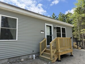 A single-story building with a front porch, a wooden bench, and a door with a number plate. - New 3BR House in Southwest Harbor! [Eagle`s Ledge] (Southwest Harbor)