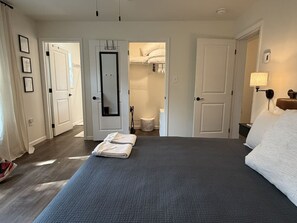 Ein Schlafzimmer mit einem großen Bett, einem Kleiderschrank, einem Spiegel und einem durch eine offene Tür einsehbaren Badezimmer.