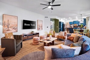 A modern living room with a flat-screen TV, comfortable seating, and a ceiling fan. - Adobe Afterglow | Swim, Soak, Play & Stay Awhile (Mesa)
