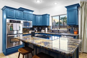 A kitchen with blue cabinets, stainless steel appliances, a granite countertop, and a window with a view. - Adobe Afterglow | Swim, Soak, Play & Stay Awhile (Mesa)