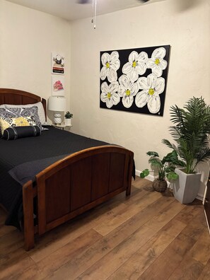 A bedroom with a wooden bed, a nightstand, a lamp, and a wall painting.