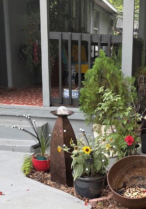 En veranda med forskellige potteplanter, en dekorativ metalkunst og en stor metalpotte på jorden.