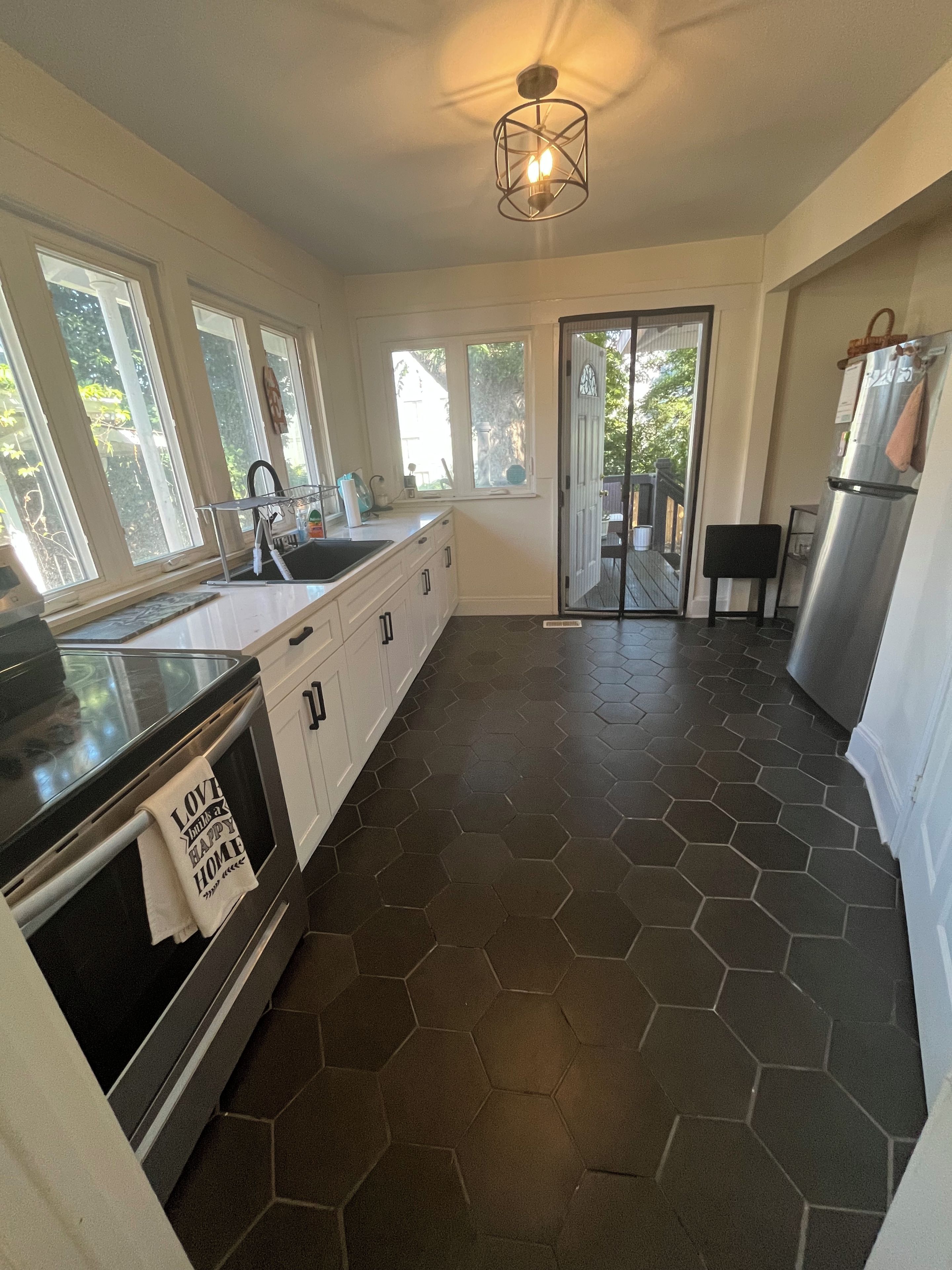 A modern kitchen with a hexagonal tile floor, stainless steel appliances, and a large window providing natural light.