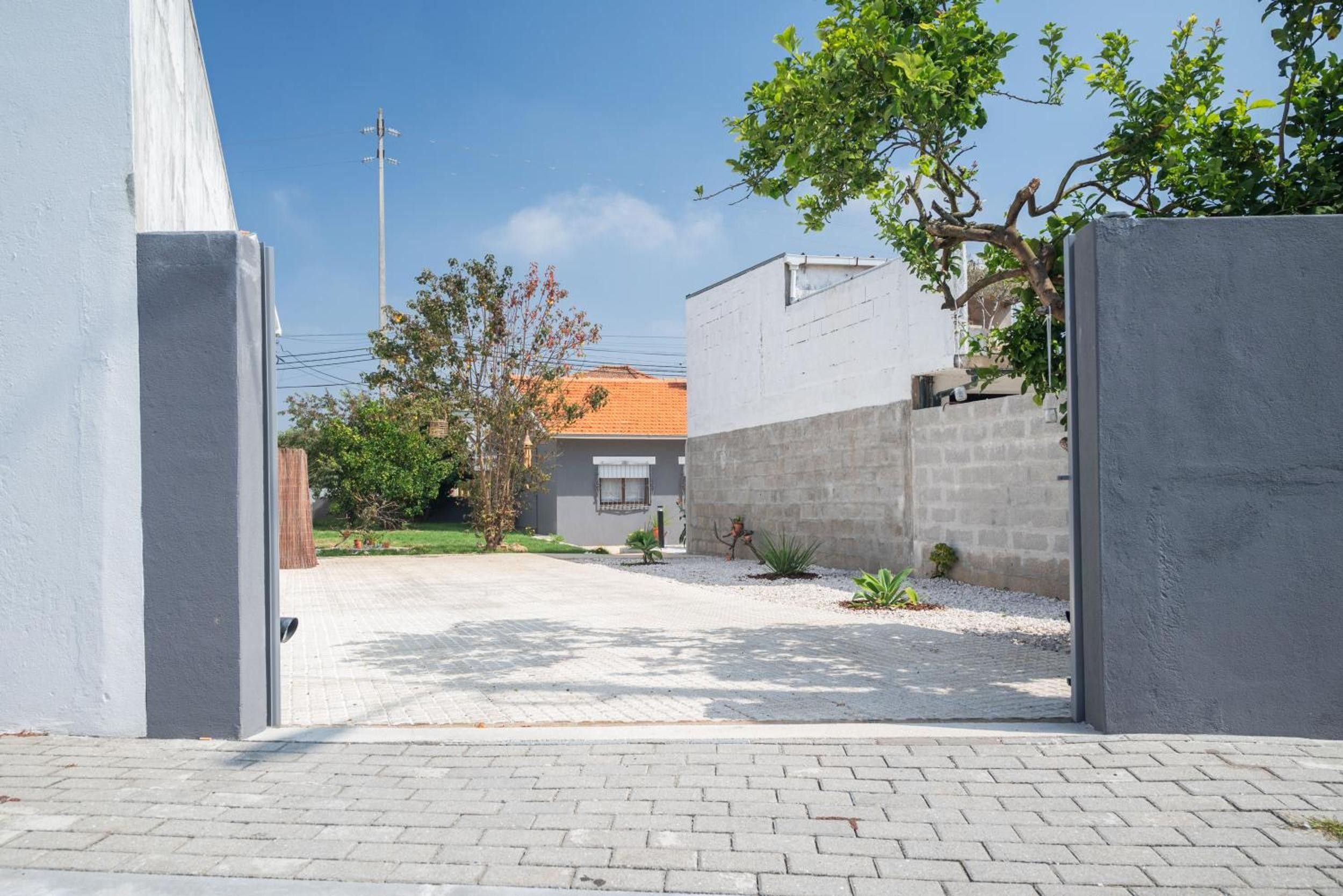 A paved driveway leading to a building with a tiled roof, surrounded by a low wall and greenery.