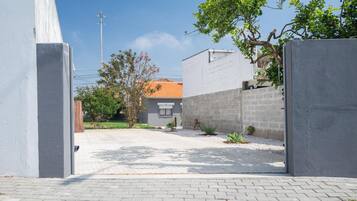 A paved driveway leading to a building with a tiled roof, surrounded by a low wall and greenery.
