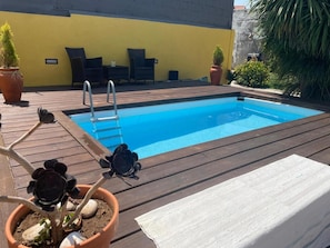 Una piscina con cubierta de madera, rodeada de plantas en macetas y mobiliario de exterior.