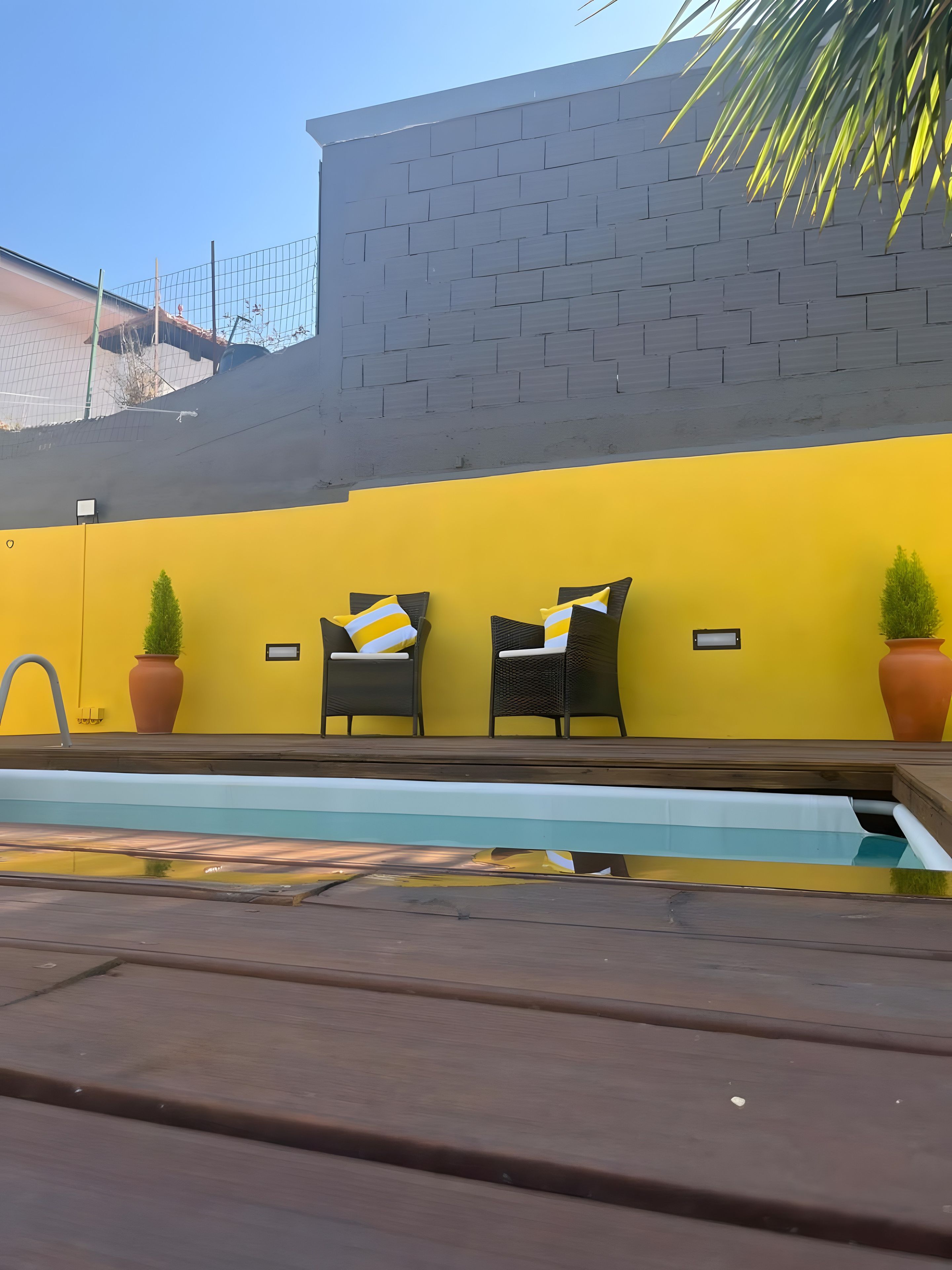 A pool area with two wicker chairs and potted plants against a yellow wall.