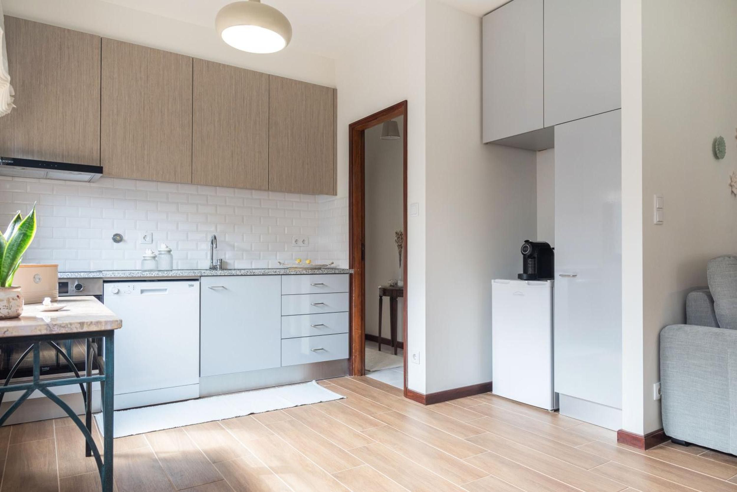 Cocina compacta con armarios blancos, lavavajillas, cafetera y comedor con mesa y sillas.
