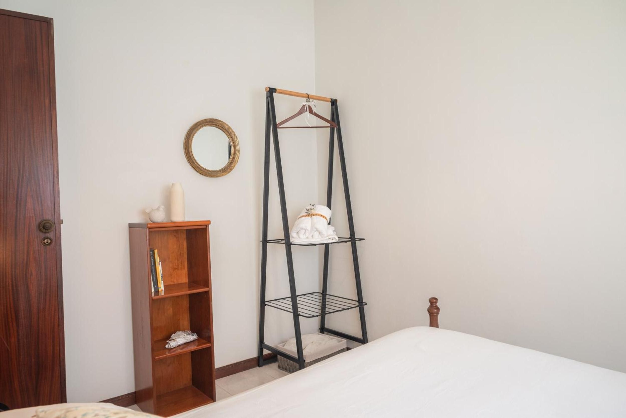 Ein Schlafzimmer mit einem Holzschrank, einer schwarzen Metallregaleinheit mit einem Handtuch und einem runden Spiegel an der Wand.