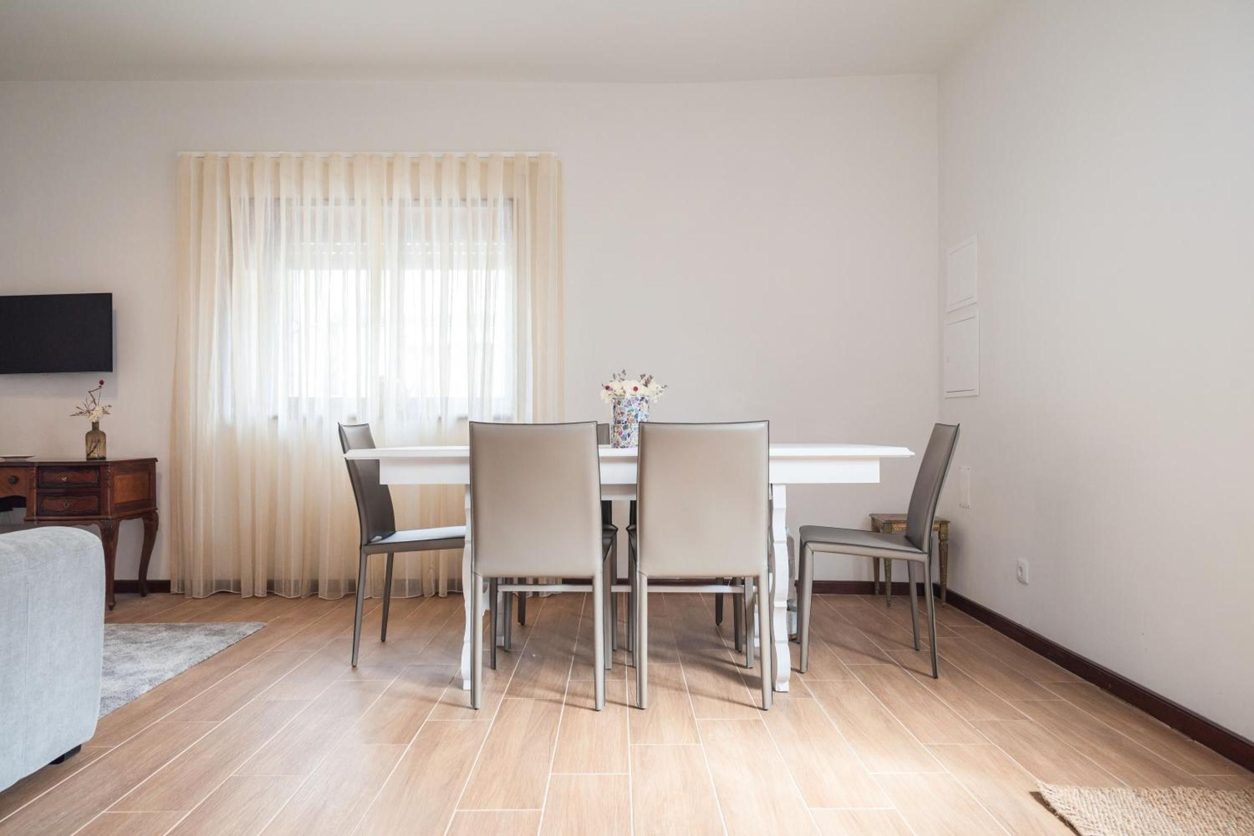 A dining area with a table and chairs, a television on the wall, and a window with curtains.