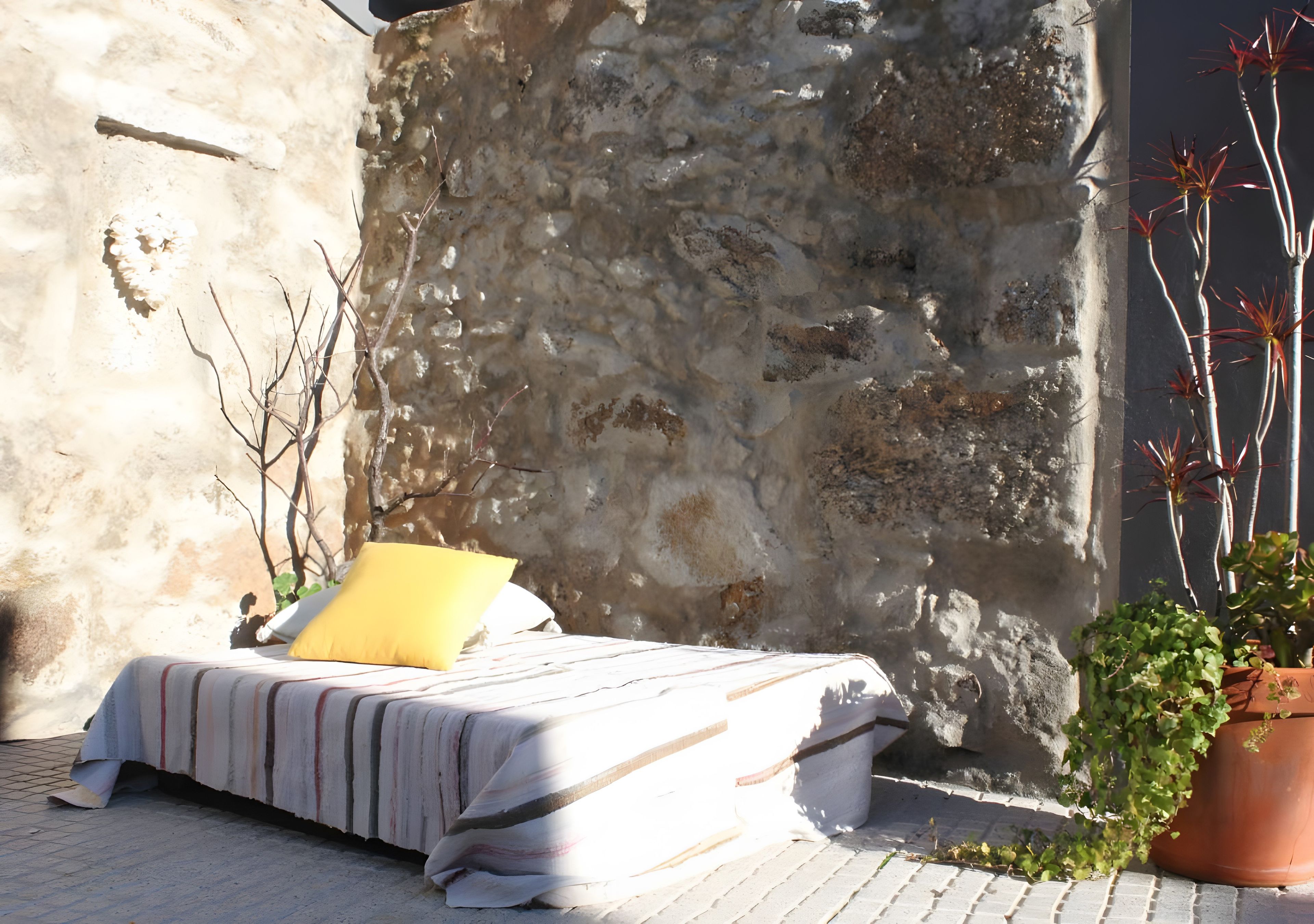 A bed with a striped bedspread and a yellow pillow in a room with a stone wall.