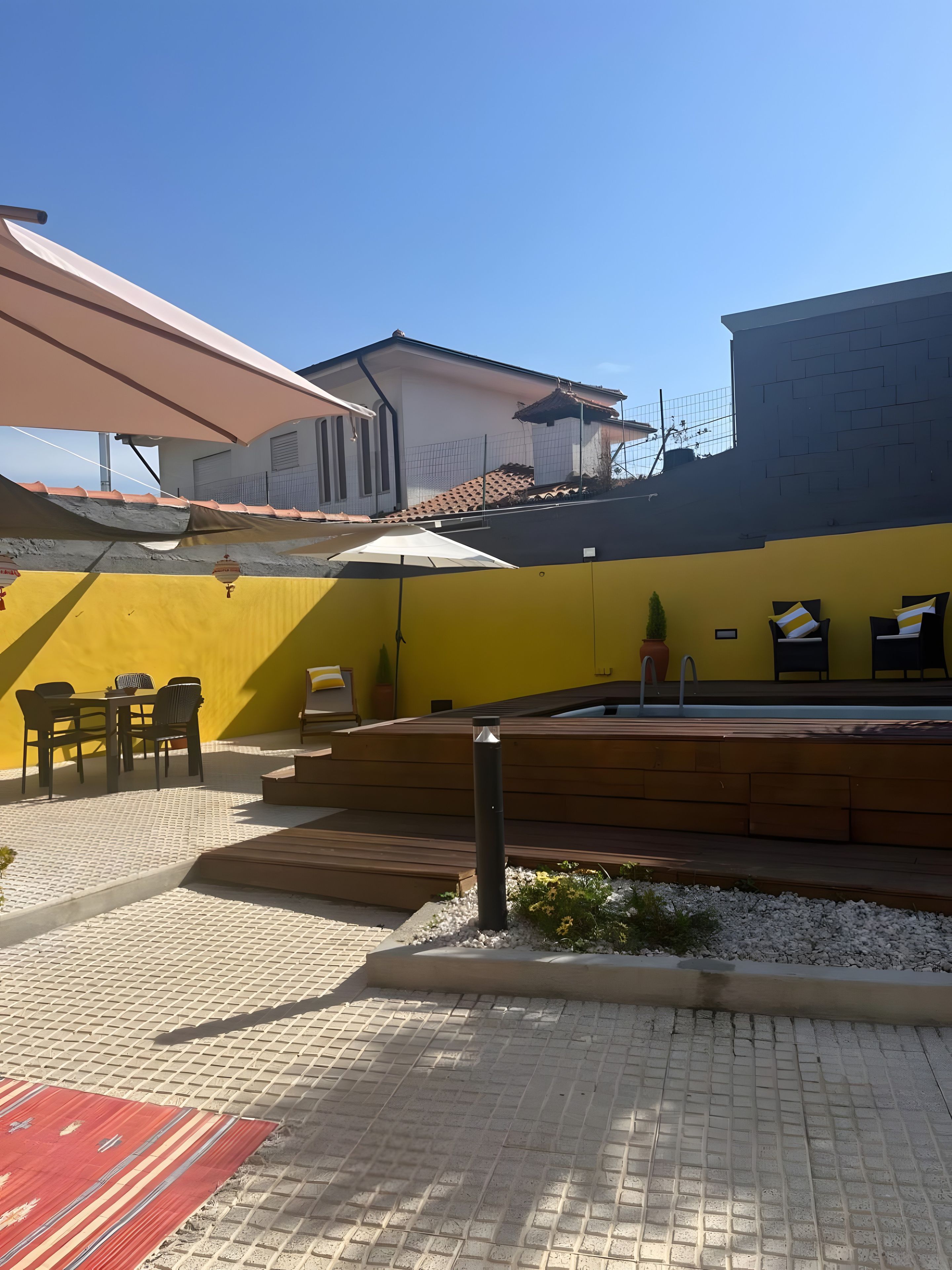 Une cour avec un mur jaune, des meubles d’extérieur et un sol carrelé.