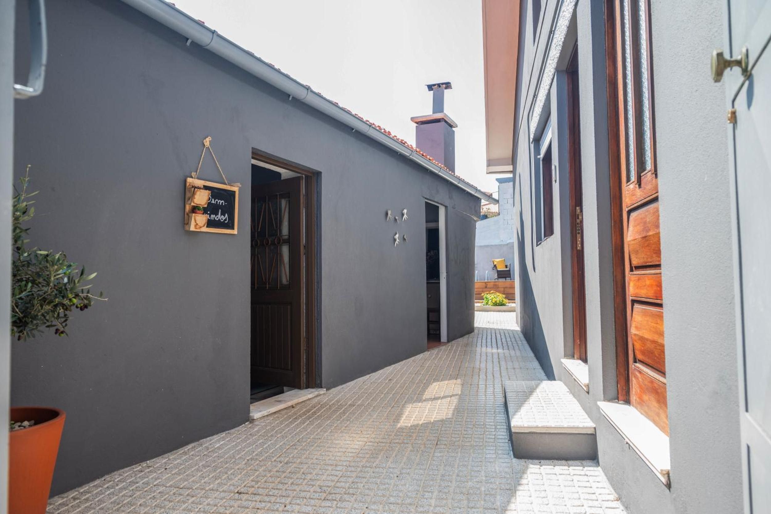 Un callejón estrecho con un edificio gris a un lado y una puerta de madera al otro.