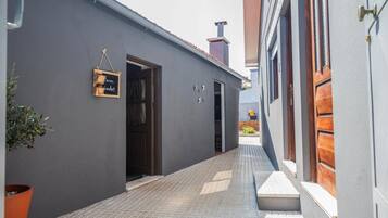 Un callejón estrecho con un edificio gris a un lado y una puerta de madera al otro.
