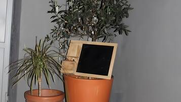 A potted plant with a small house model, two terracotta pots, and a wooden box on a tiled surface.