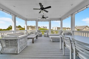 Una terraza techada al aire libre con asientos y ventiladores de techo, con vistas a una zona residencial.