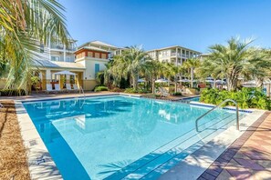 Ein Swimmingpool mit Liegestühlen und Sonnenschirmen, umgeben von Palmen und Gebäuden.