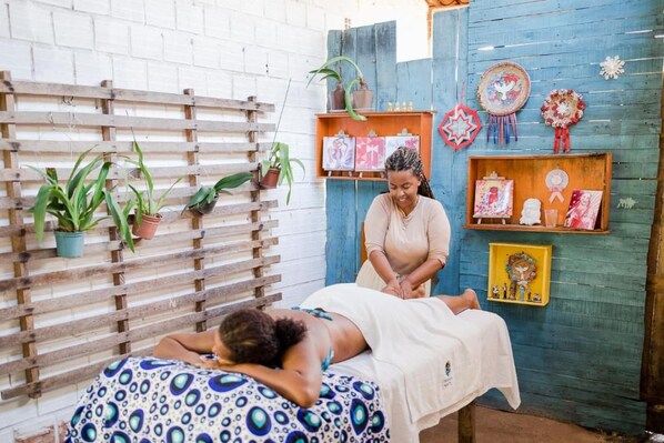A room with a wooden bed, a massage table, and a blue wall with shelves containing decorative items.