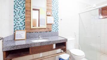 Un baño con encimera de granito, tocador de madera, lavabo blanco, espejo y cabina de ducha de vidrio.