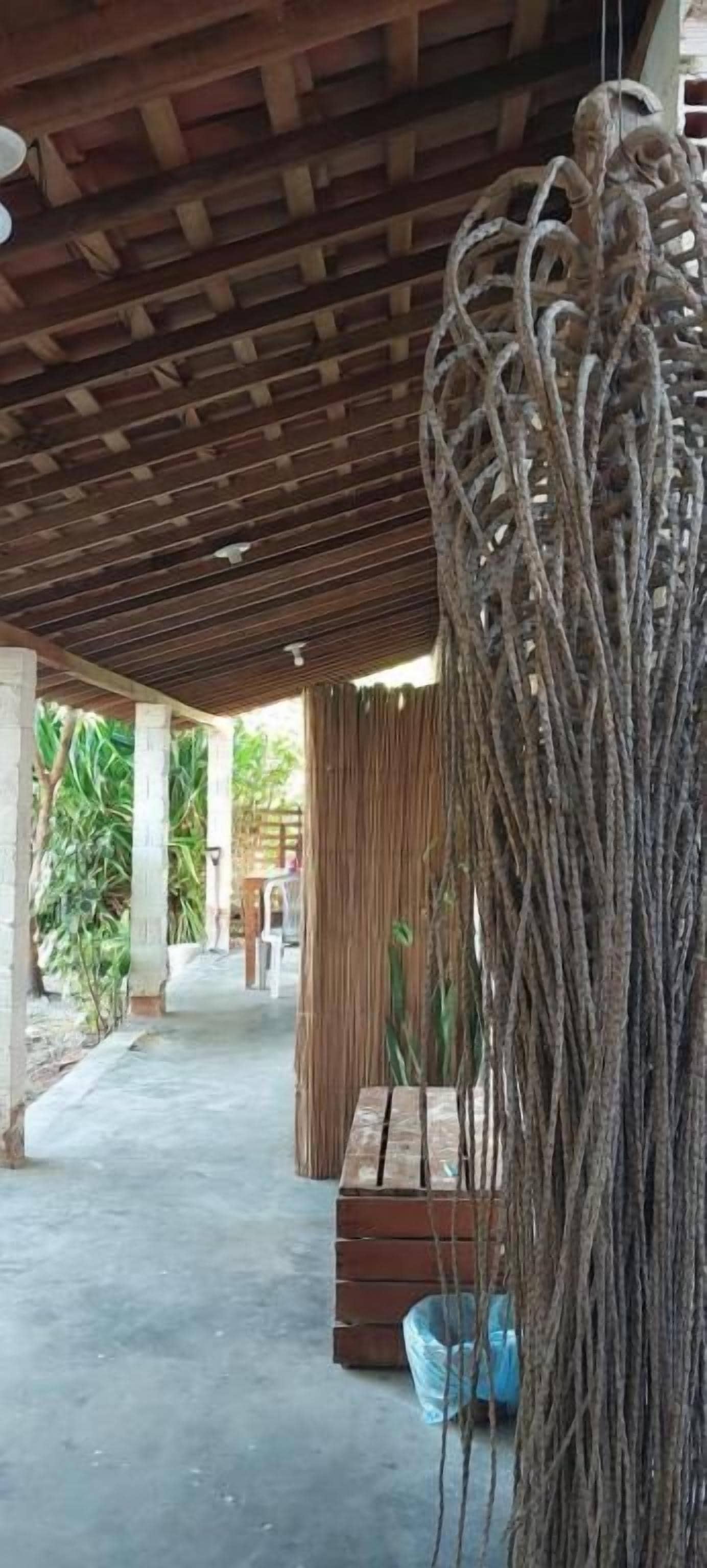 A covered outdoor area with a concrete floor, wooden ceiling beams, and a hanging rope decoration.