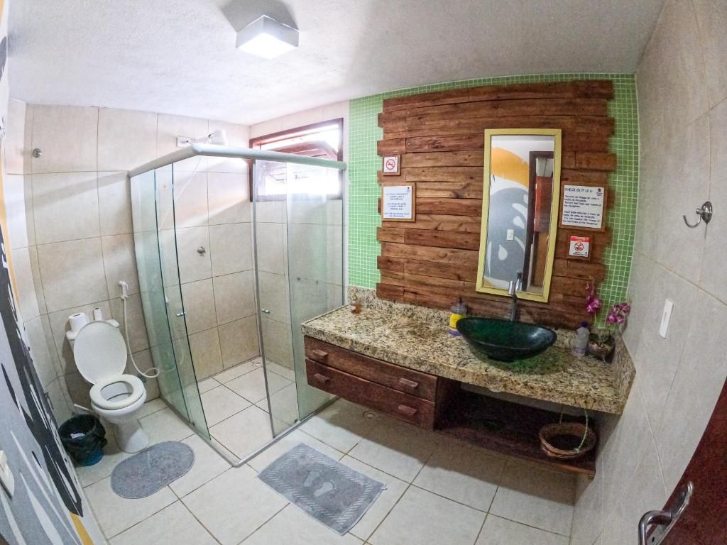 A bathroom with a glass shower enclosure, a toilet, a sink with a green basin, and a wooden vanity.