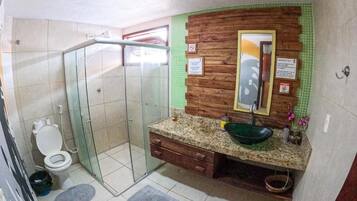 A bathroom with a glass shower enclosure, a toilet, a sink with a green basin, and a wooden vanity.