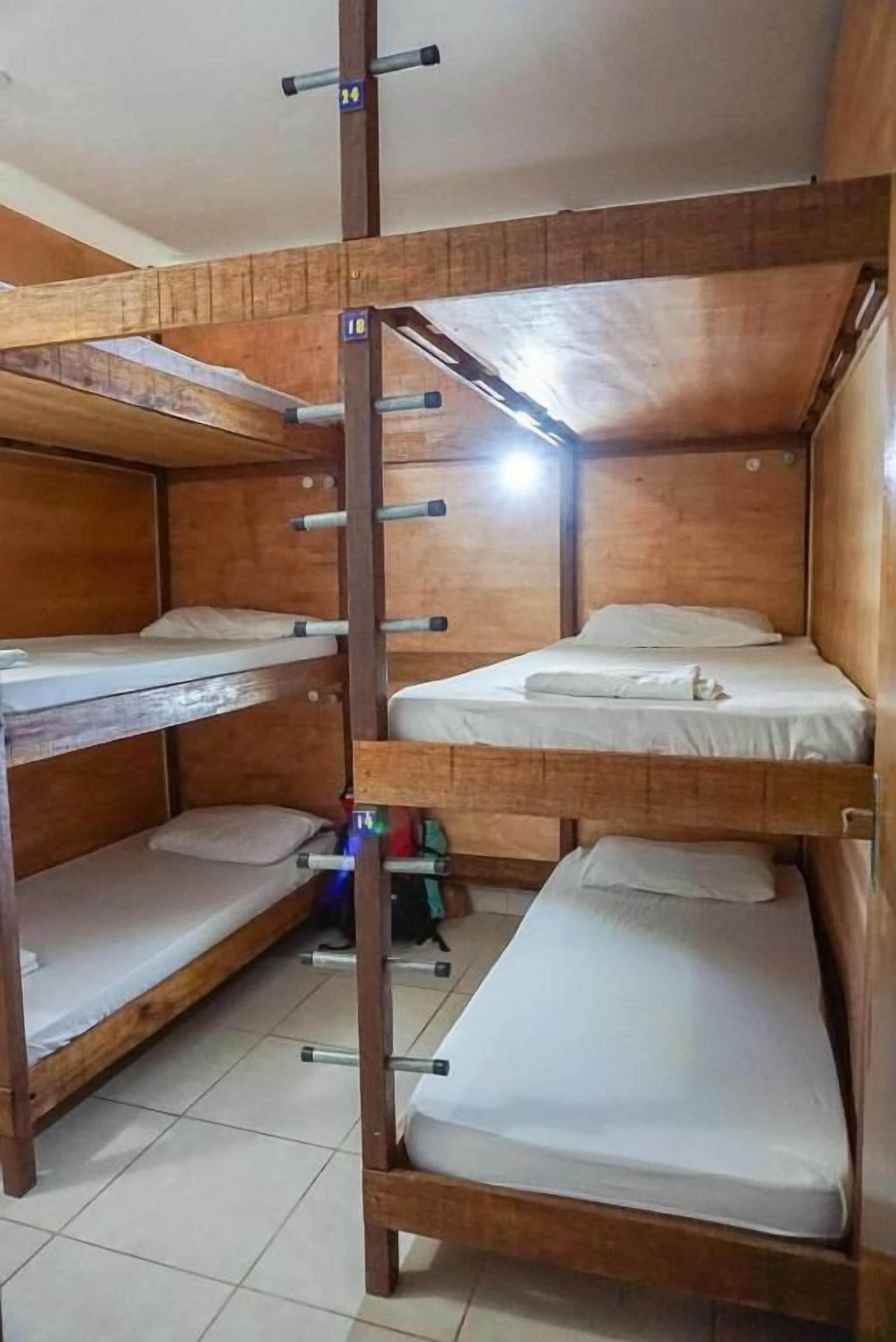 Quarto com beliche de madeira, barra de exercícios e um pequeno espaço para guardar pertences.