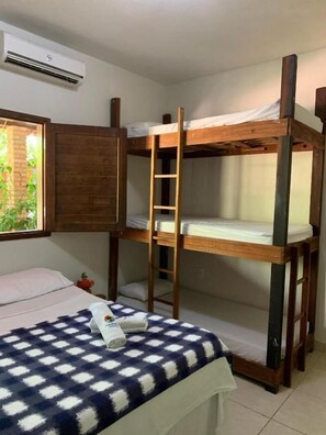 A bunk bed room with a ladder, a checkered bedspread, and a window with a view of greenery.