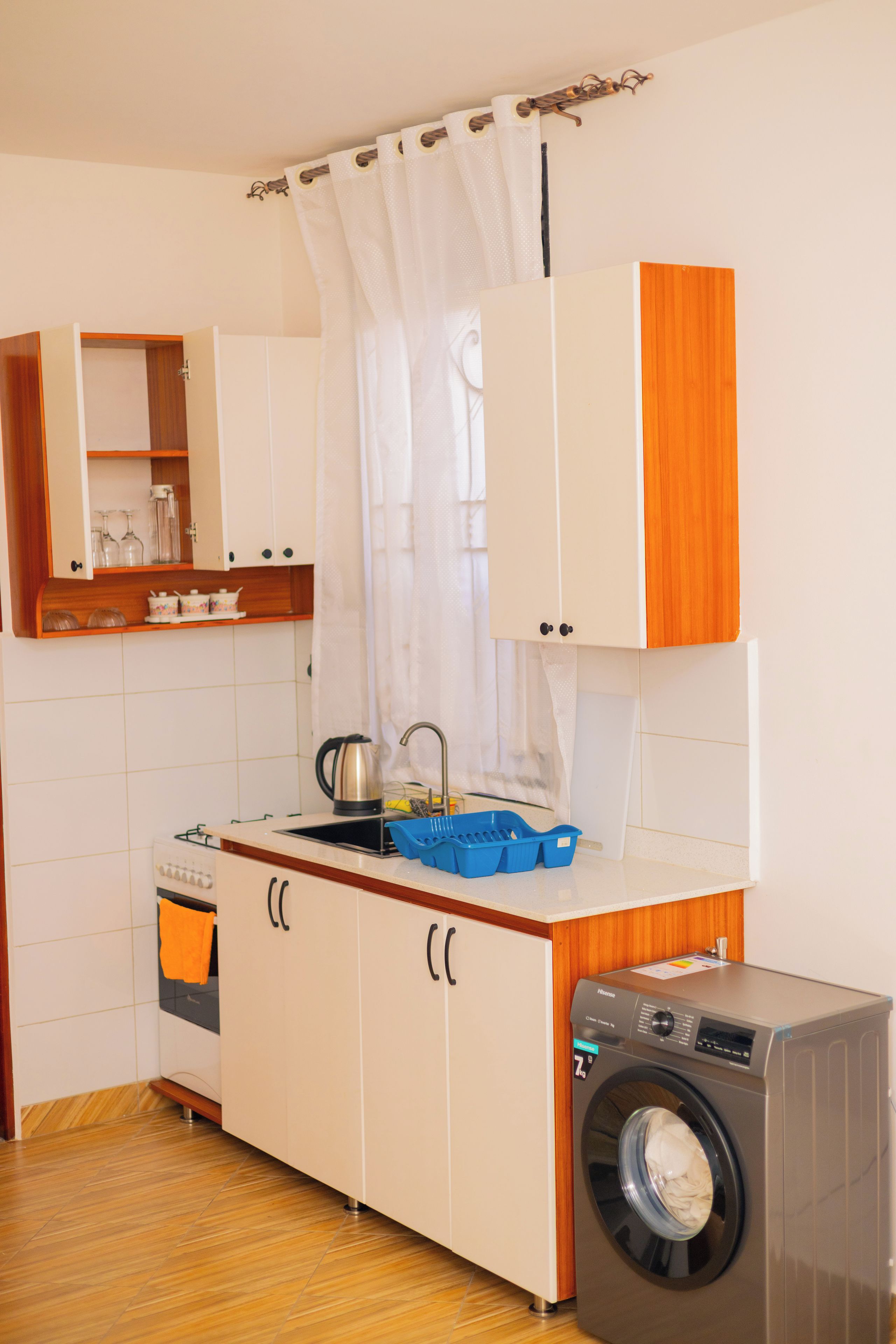 Une petite cuisine équipée d’un lave-linge, d’un évier et d’un meuble contenant de la vaisselle et des verres.