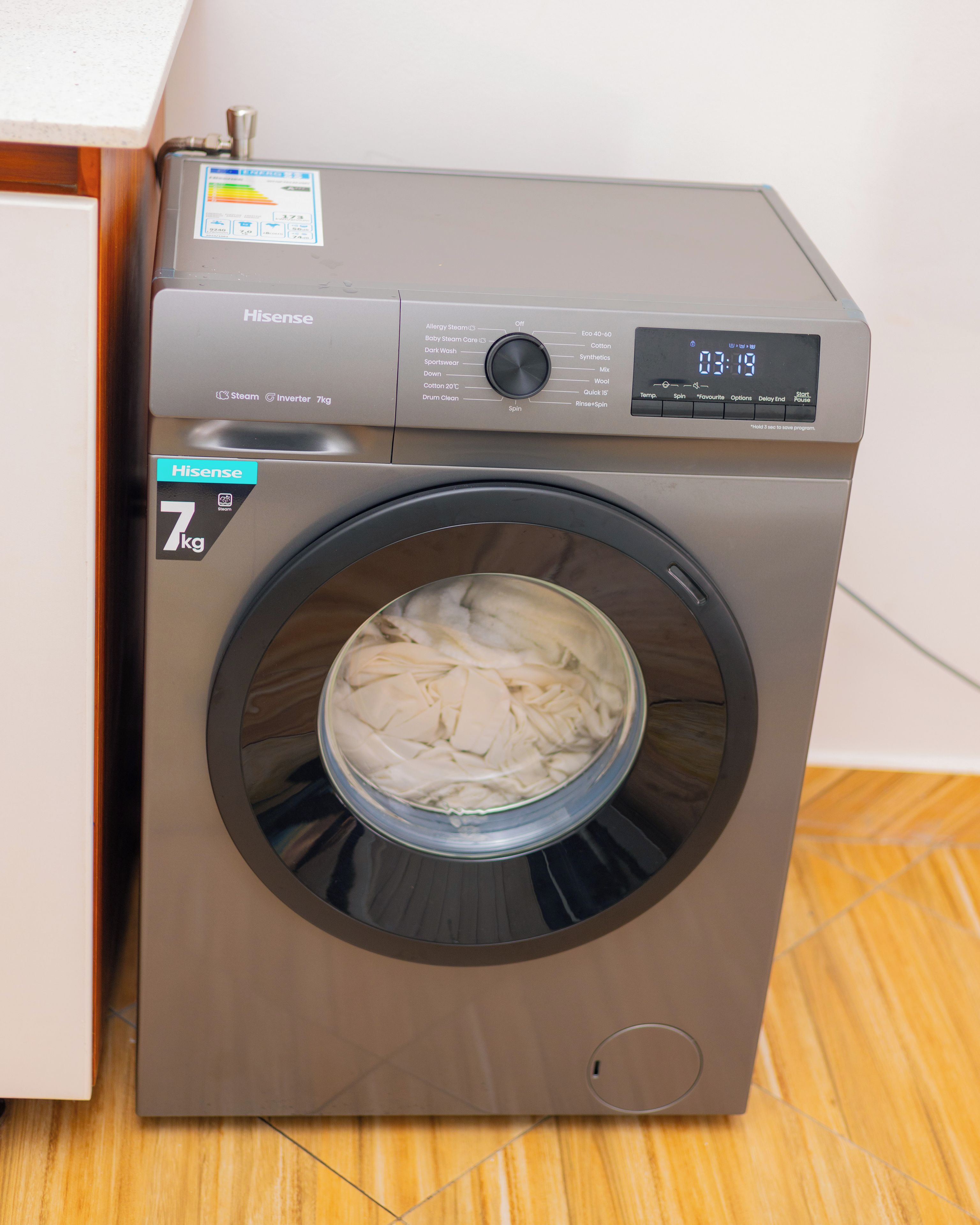 Una lavatrice a carica frontale Hisense da 7 kg con display digitale, pannello di controllo e oblò in vetro.