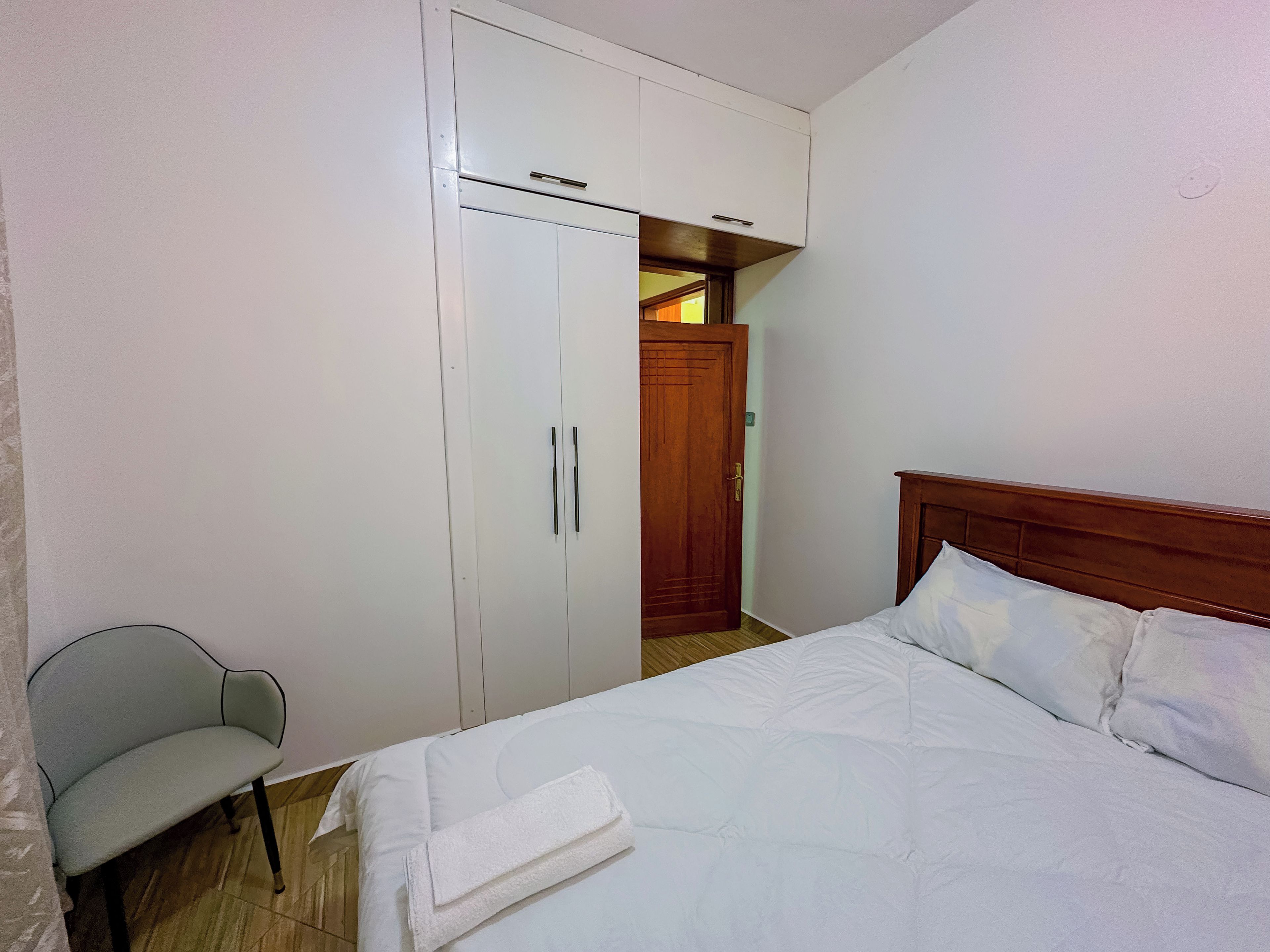 Una camera d'albergo con un letto, una sedia, un armadio e una porta che dà su un'altra stanza.