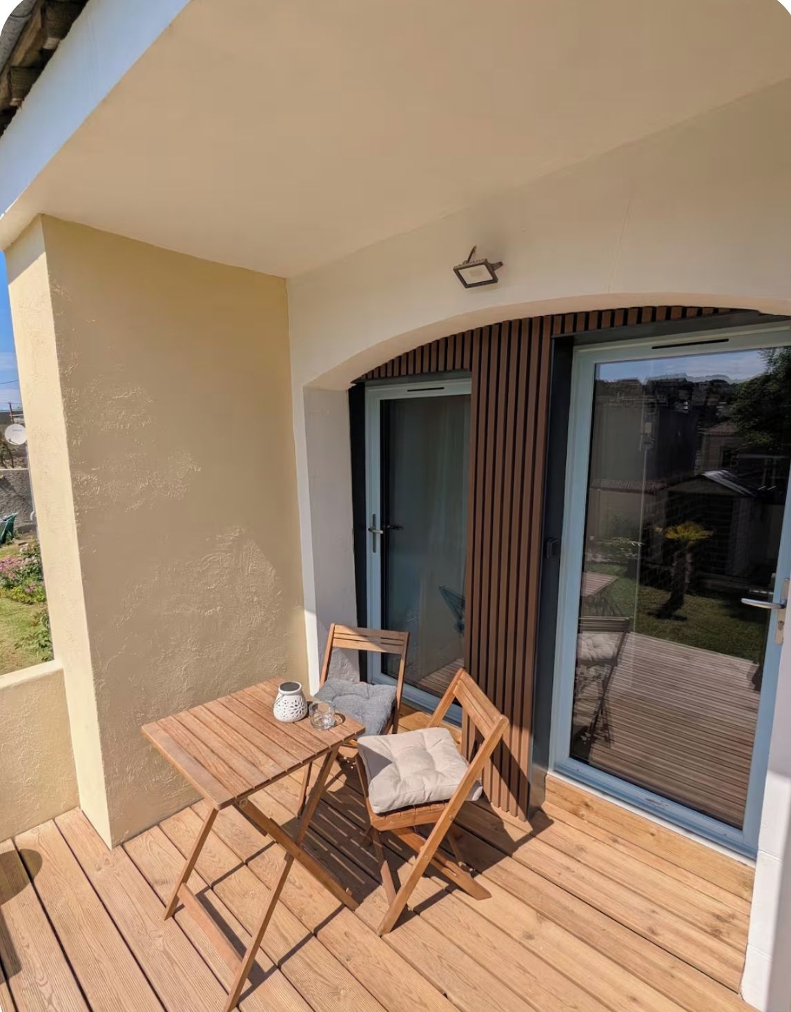 A wooden deck with a table and chairs, a sliding glass door, and a small outdoor area with a view of the surrounding landscape.