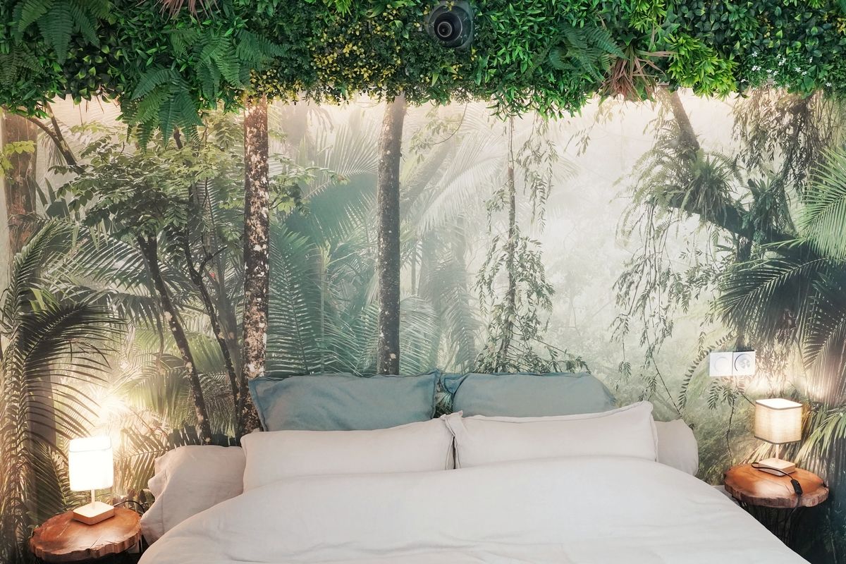 Ein Bett mit weißer Matratze, zwei Kissen und einem Kopfteil mit einem Wald-Mural. Es gibt zwei Nachttische mit Lampen.