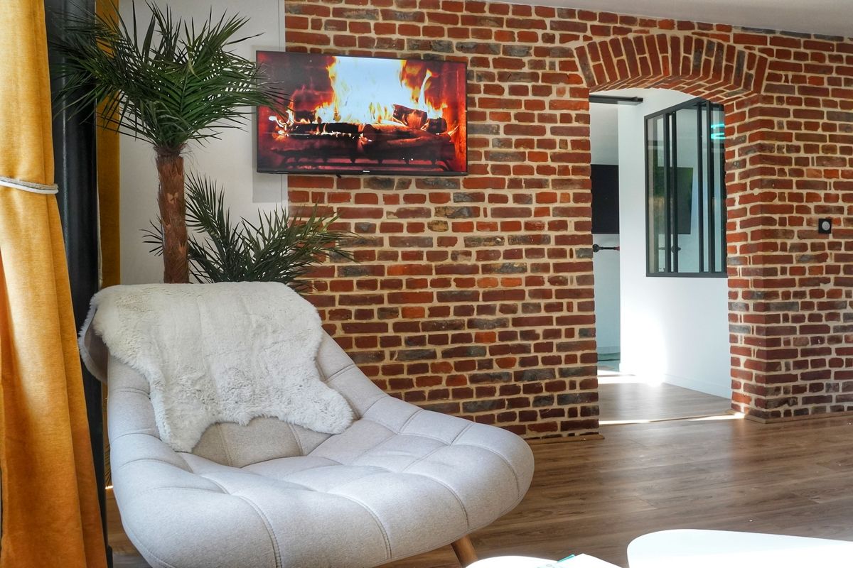Ein modernes Wohnzimmer mit Backsteinwand, Flachbildfernseher, weißem Sessel und einer Topfpflanze.